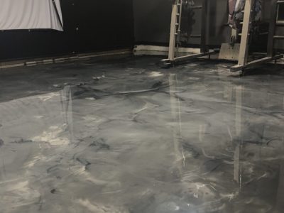 A gym room with weightlifting equipment and a polished, marbled gray epoxy floor.